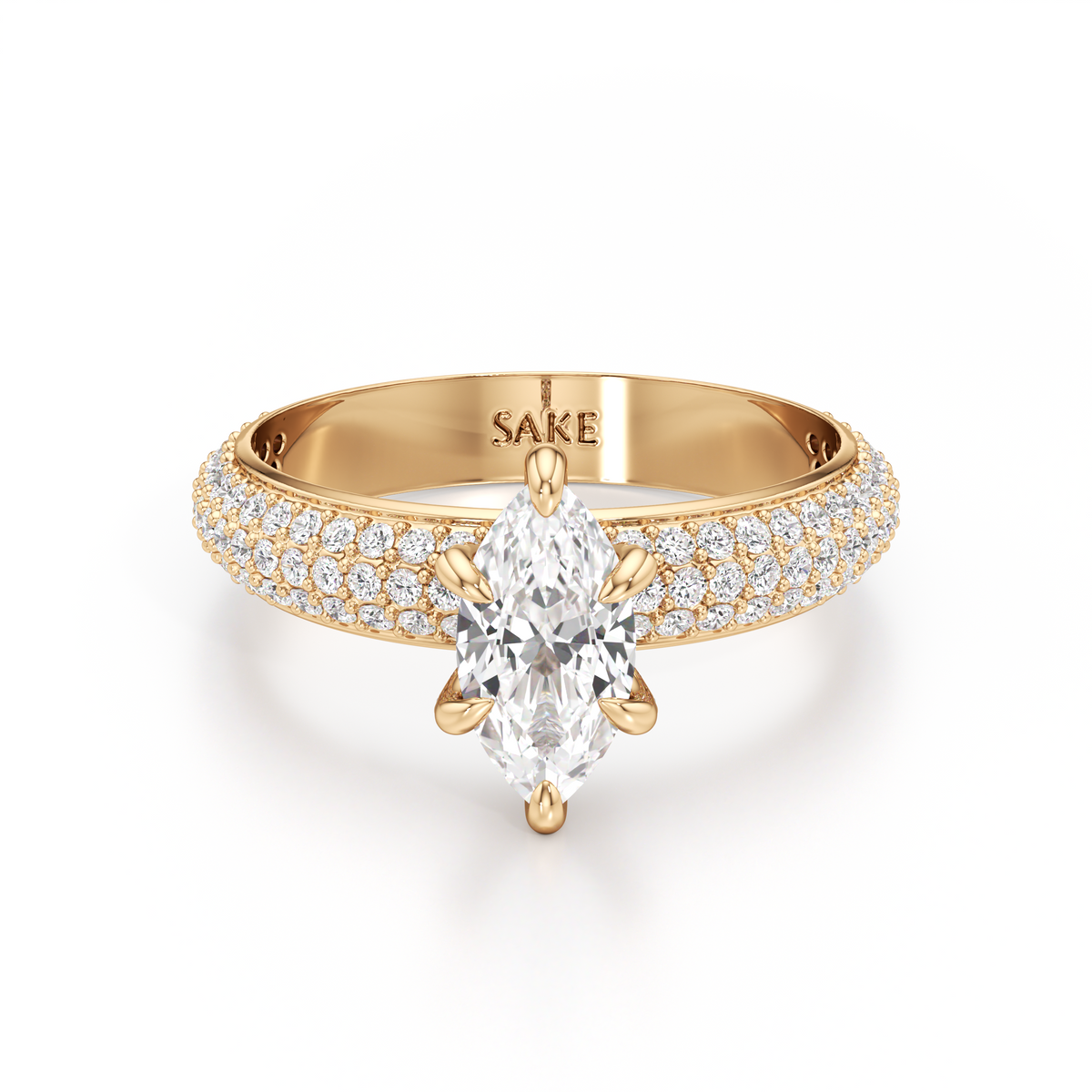 A yellow gold engagement ring featuring a marquise-cut clear center stone and pavé-set diamonds along the shoulders, shown on a clean white background. The inside of the band is engraved with the brand name 'SAKE'.