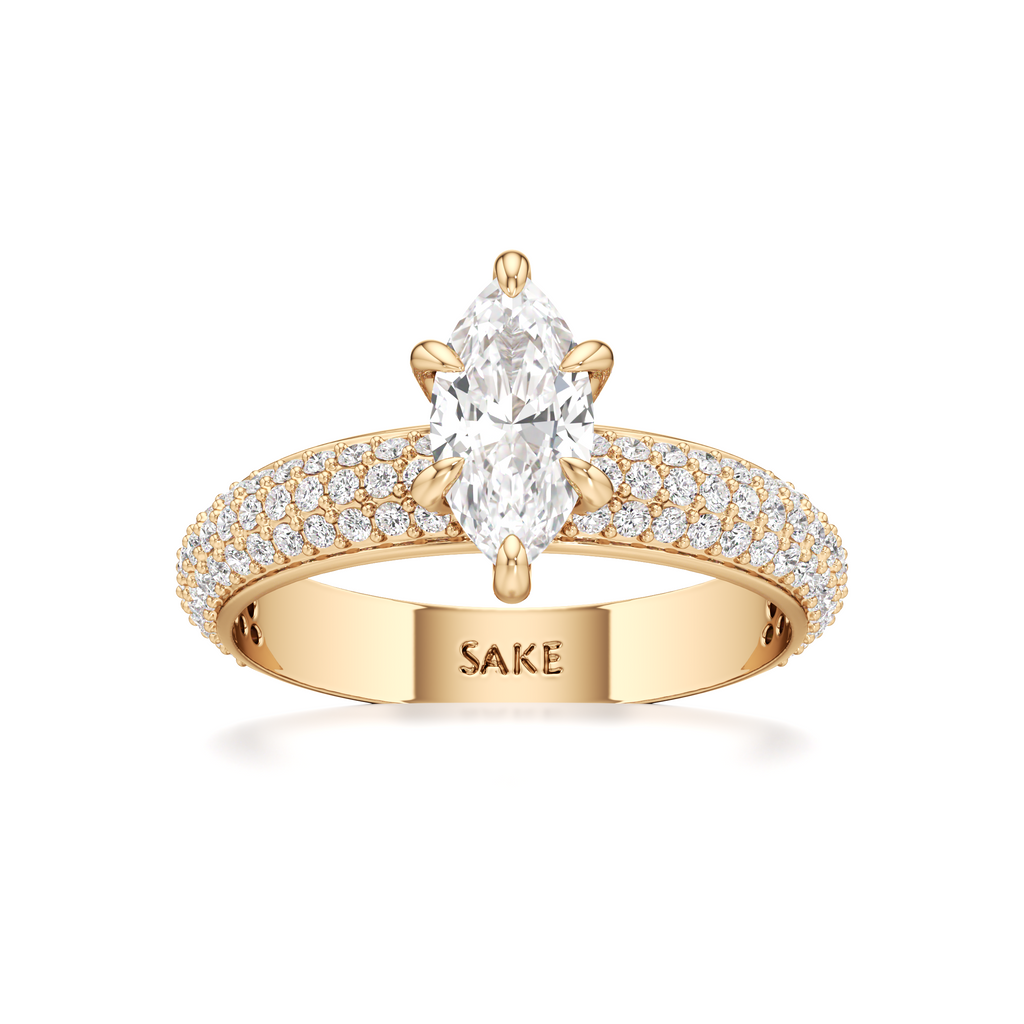 A yellow gold ring featuring a large oval-cut center stone and a pavé-set band with small clear stones. The inside of the band is engraved with the brand name 'SAKE'.