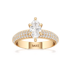 A yellow gold ring featuring a large oval-cut center stone and a pavé-set band with small clear stones. The inside of the band is engraved with the brand name 'SAKE'.