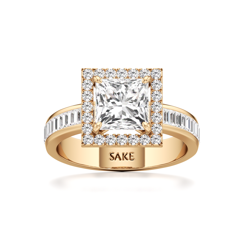 A yellow gold ring with a princess-cut diamond center stone and a halo of smaller diamonds, featuring a band with baguette and round diamonds. The inside of the band is engraved with the brand name 'SAKE'.