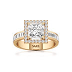 A yellow gold ring with a princess-cut diamond center stone and a halo of smaller diamonds, featuring a band with baguette and round diamonds. The inside of the band is engraved with the brand name 'SAKE'.
