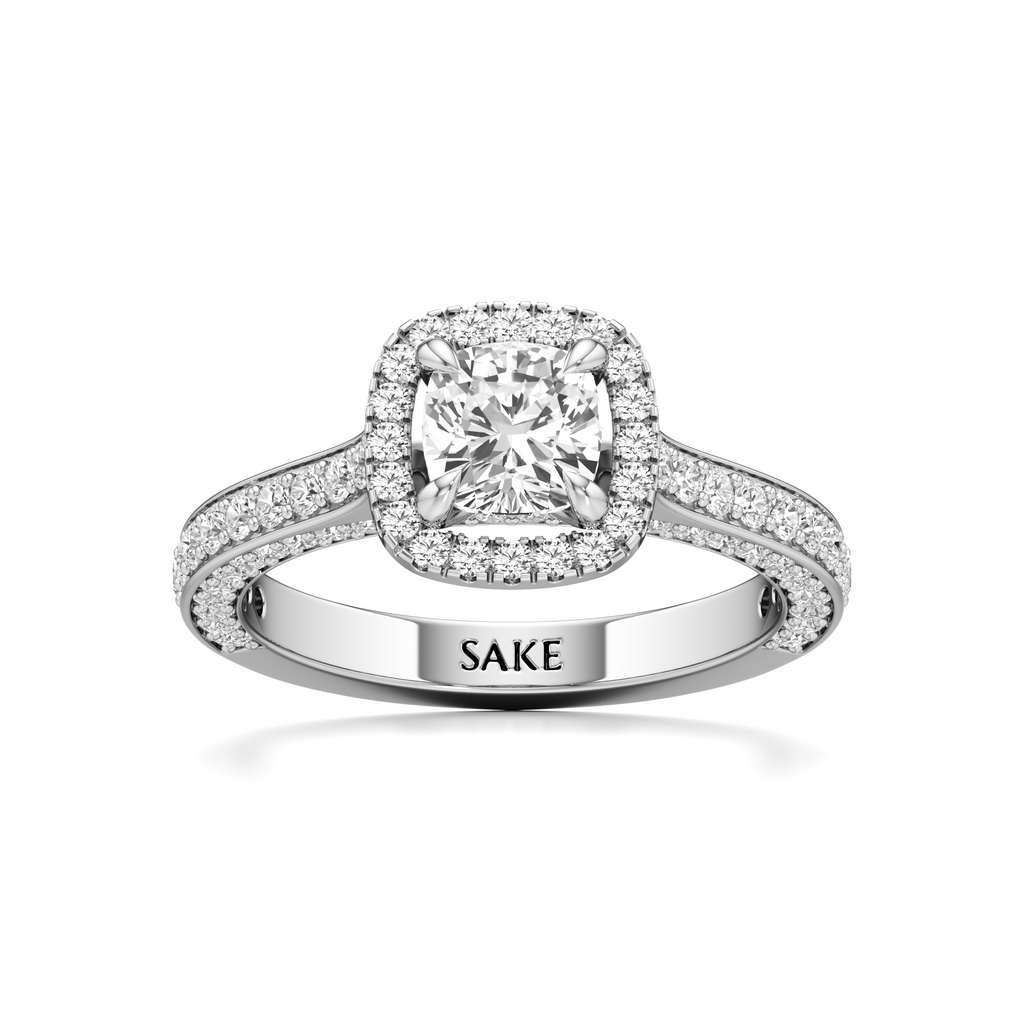 A silver-toned halo engagement ring with a cushion-cut center diamond and pavé-set band, featuring the engraved brand name 'SAKE' on the inside of the band, set against a plain white background.