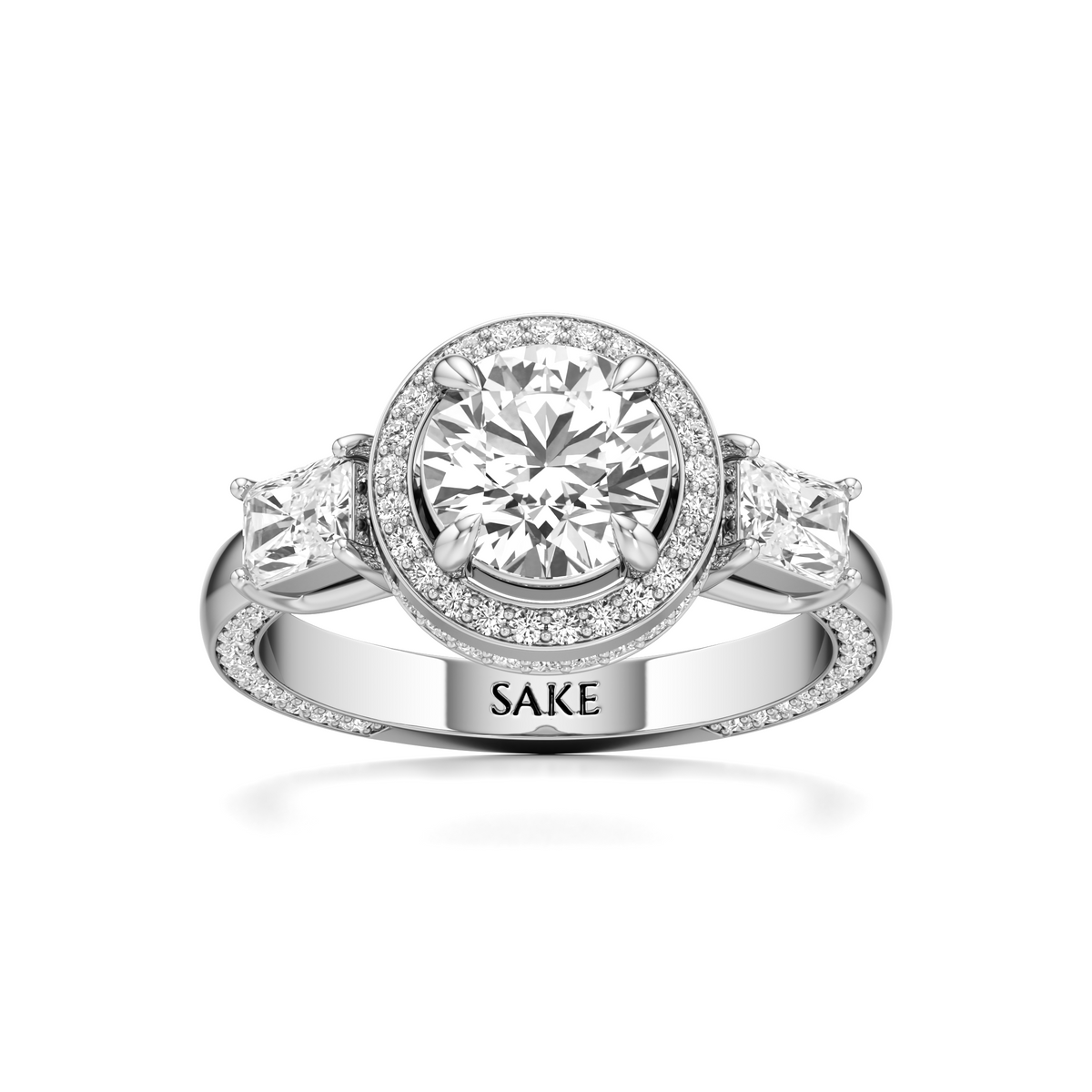 A silver-toned diamond ring with a round-cut center stone, a halo of small diamonds, and three marquise-cut side stones. The band is engraved with the name 'SAKE'.