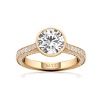 A yellow gold solitaire engagement ring featuring a round brilliant-cut diamond center stone and a pavé-set diamond band, with the brand name 'SAKE' engraved on the inner band, set against a clean white background.