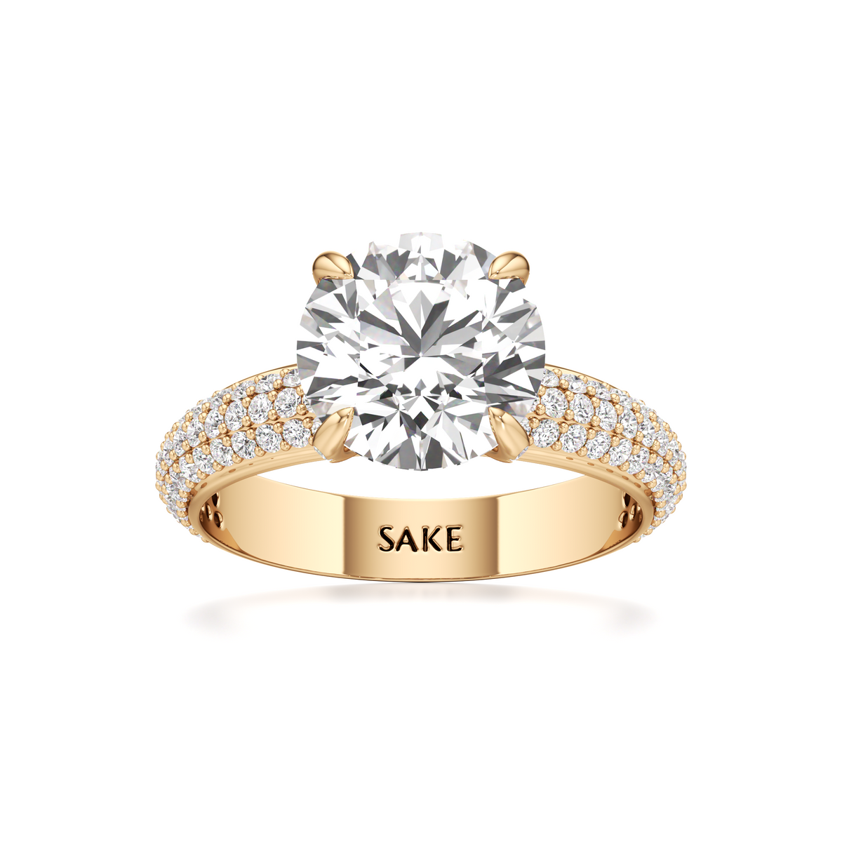 A yellow gold solitaire engagement ring with a round-cut diamond center stone and pavé-set diamonds on the band, featuring the engraved brand name 'SAKE' on the inside of the band.