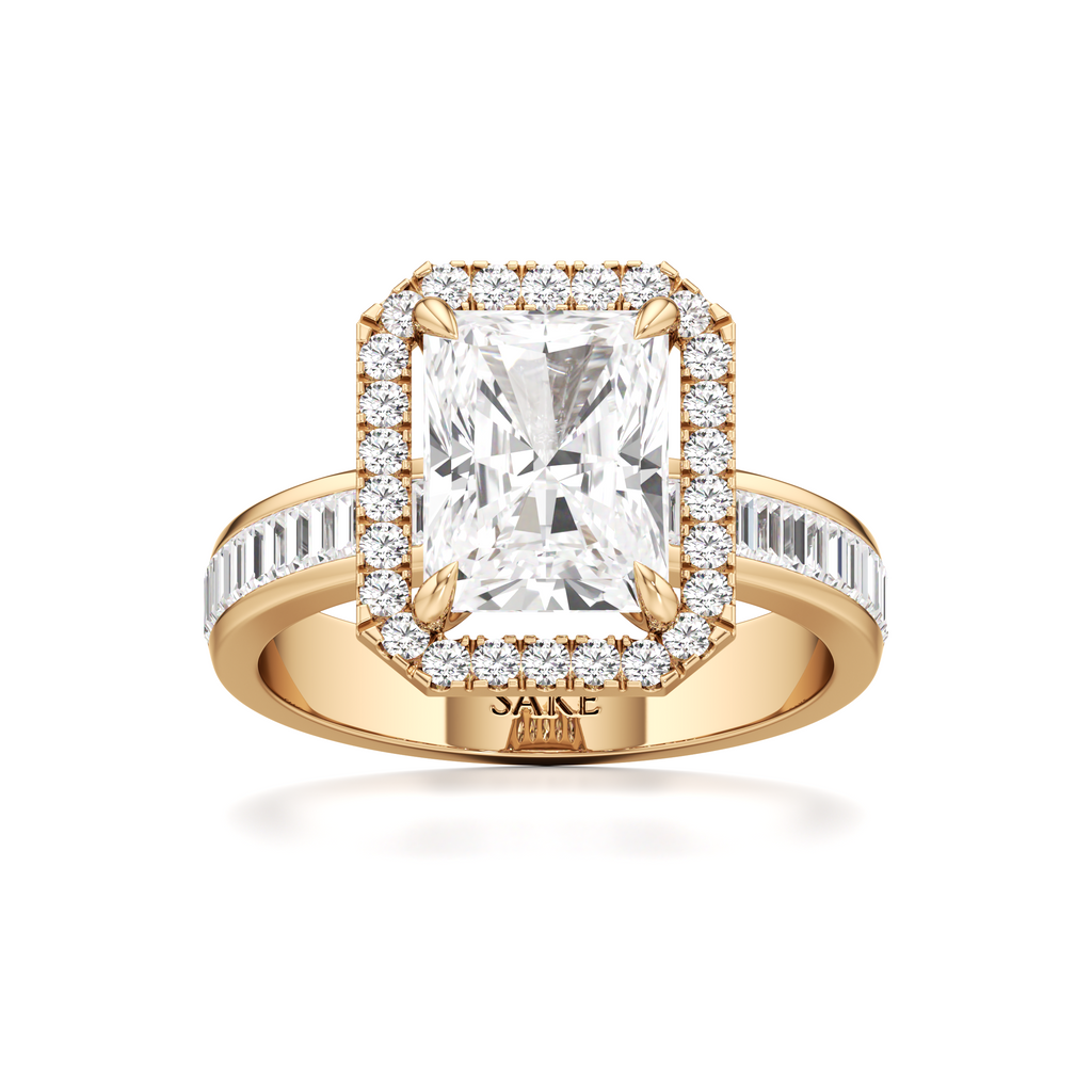 A yellow gold ring with a large rectangular emerald-cut center stone surrounded by a halo of small clear stones, and a channel-set stone band, shown on a white background. The inside of the band is stamped with 'SAKE'.