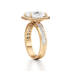 A yellow gold engagement ring featuring a large cushion-cut diamond center stone in a prong setting, with a shank paved with baguette diamonds, shown on a white background.