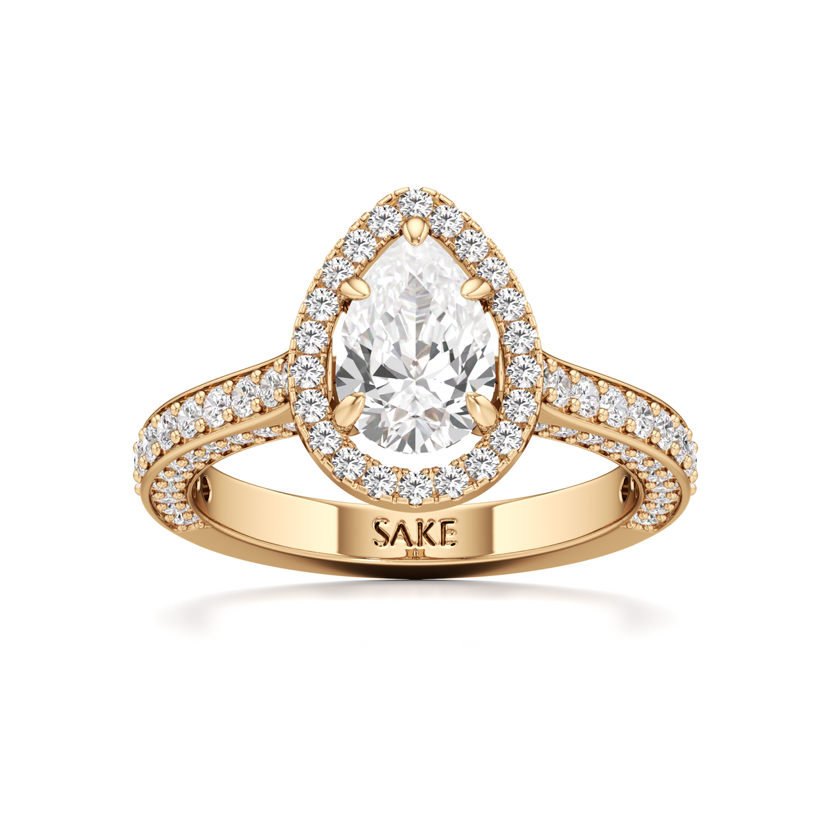 A yellow gold pear-cut diamond engagement ring with a halo of small diamonds and a split shank engraved with the brand name 'SAKE'.