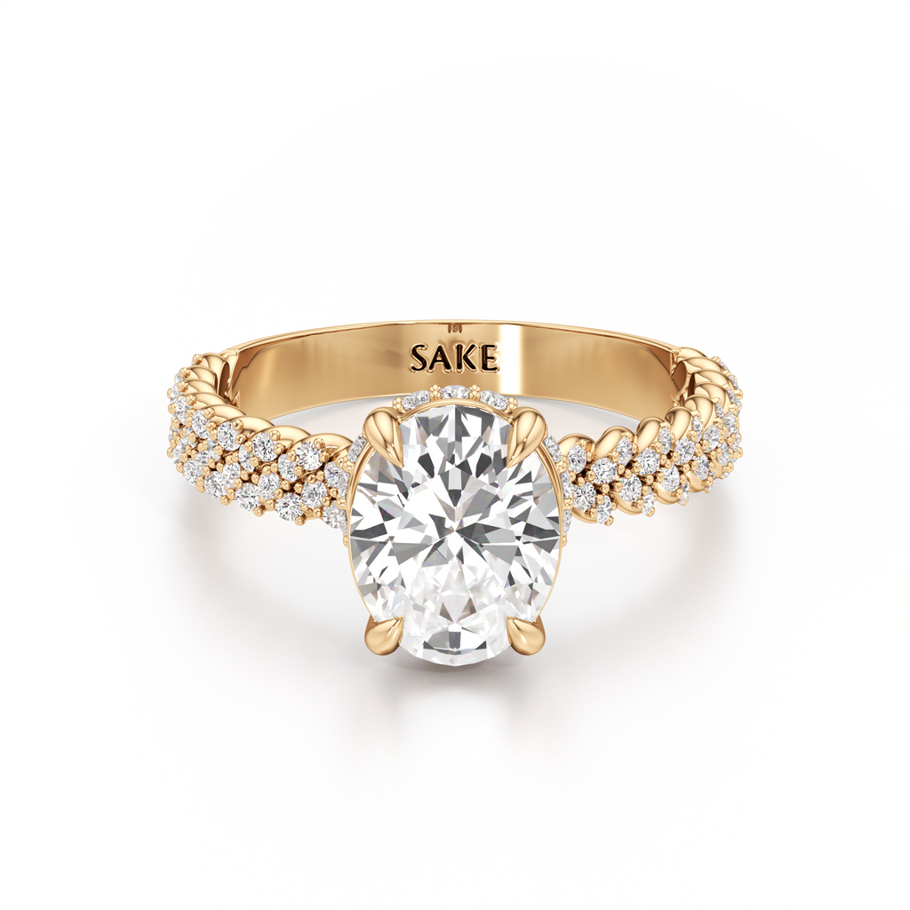 A yellow gold engagement ring featuring a large oval-cut center diamond and pavé-set diamonds along the shank, with the brand name 'SAKE' engraved inside the band, shown on a clean white background.