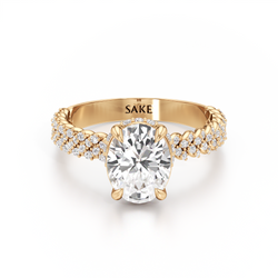 A yellow gold engagement ring featuring a large oval-cut center diamond and pavé-set diamonds along the shank, with the brand name 'SAKE' engraved inside the band, shown on a clean white background.