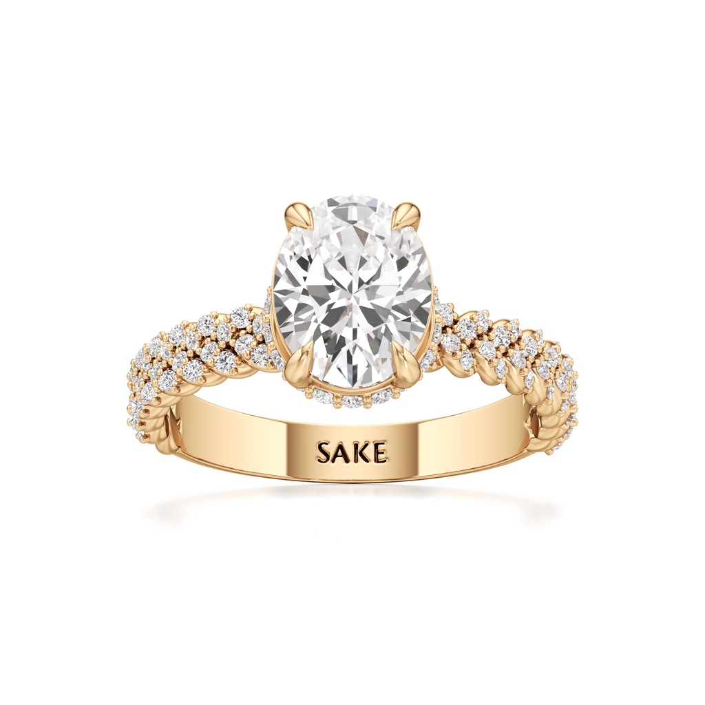 A yellow gold engagement ring featuring a large round-cut diamond center stone and a pavé-set diamond band, with the brand name 'SAKE' engraved on the inner band, set against a plain white background.