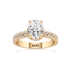A yellow gold engagement ring featuring a large round-cut diamond center stone and a pavé-set diamond band, with the brand name 'SAKE' engraved on the inner band, set against a plain white background.